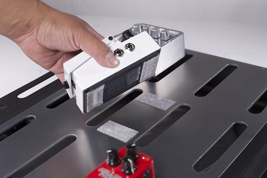 Guitar effects pedal being pressed onto a slotted pedalboard fitted with fastener strips
