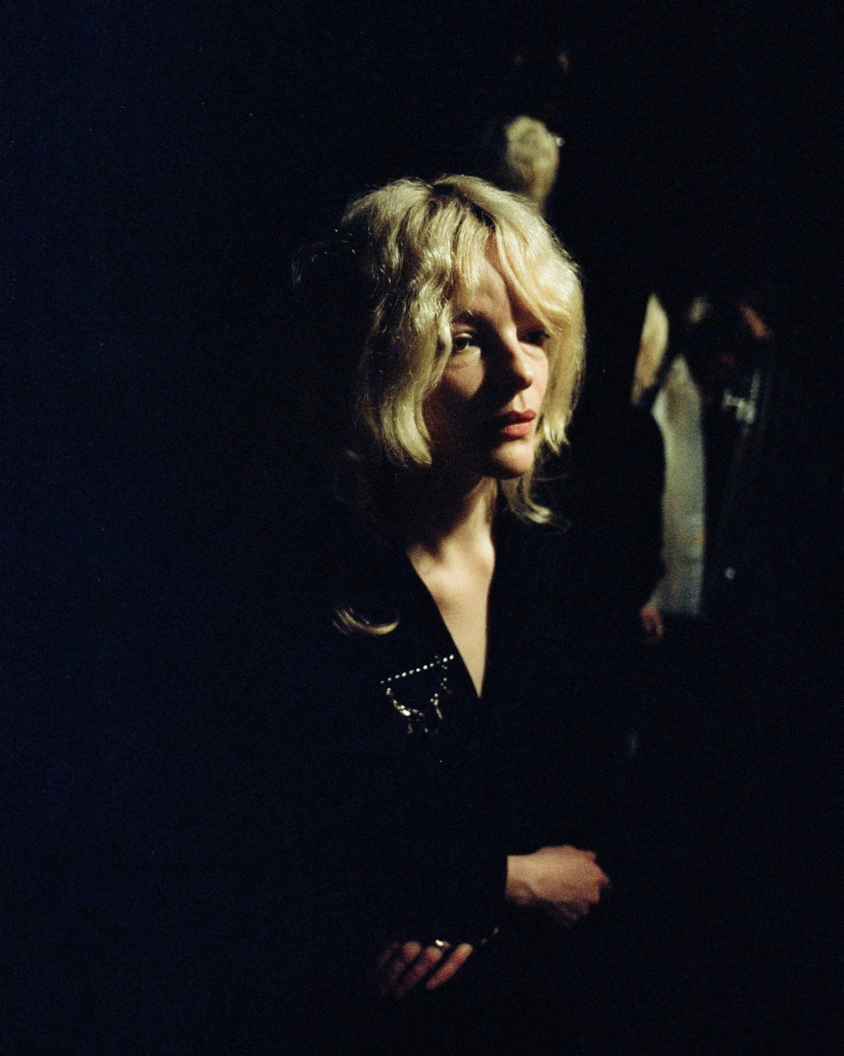 Blonde woman in a black jacket, half lit in a dark room