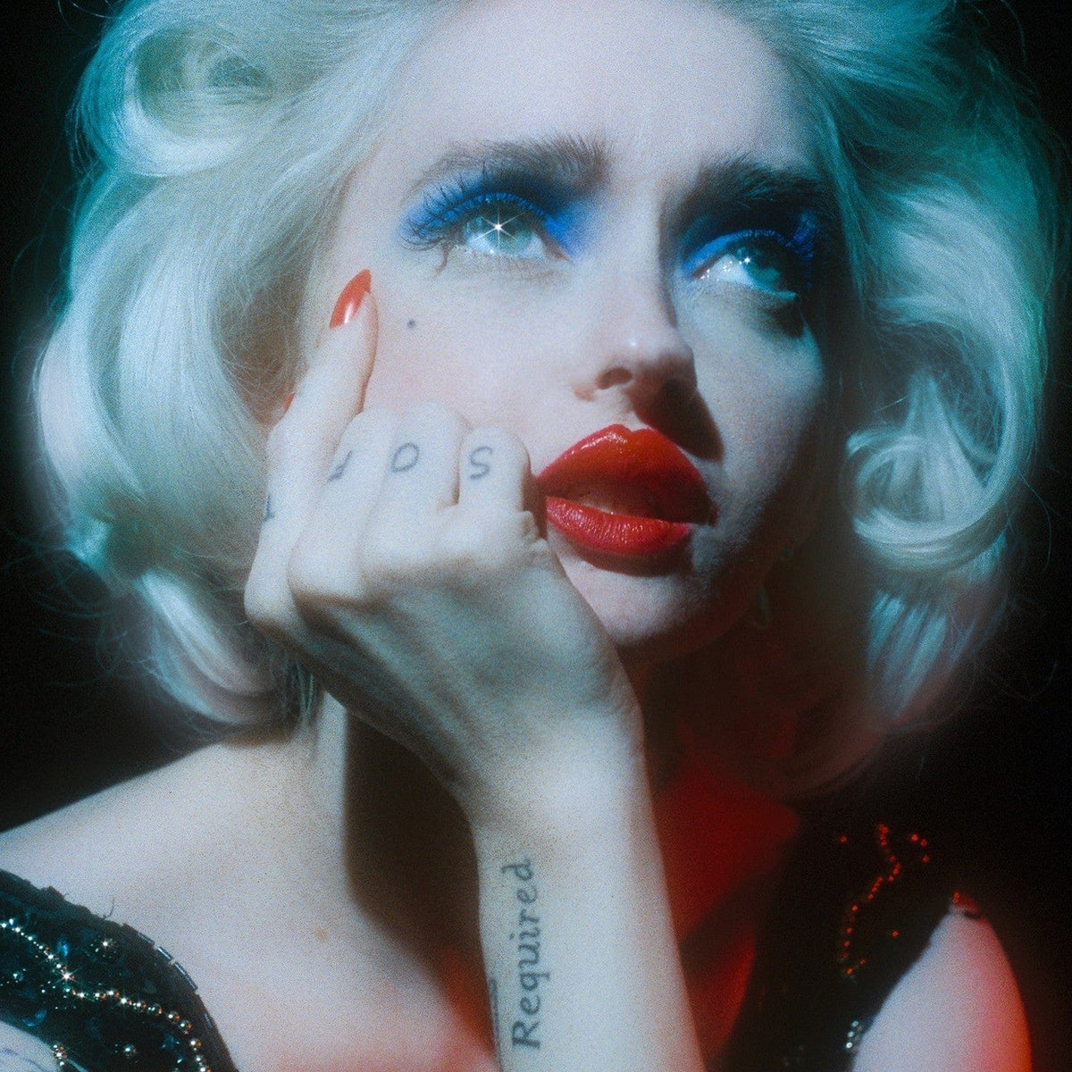Woman with platinum hair, blue eyeshadow and red nails resting her chin on her hand