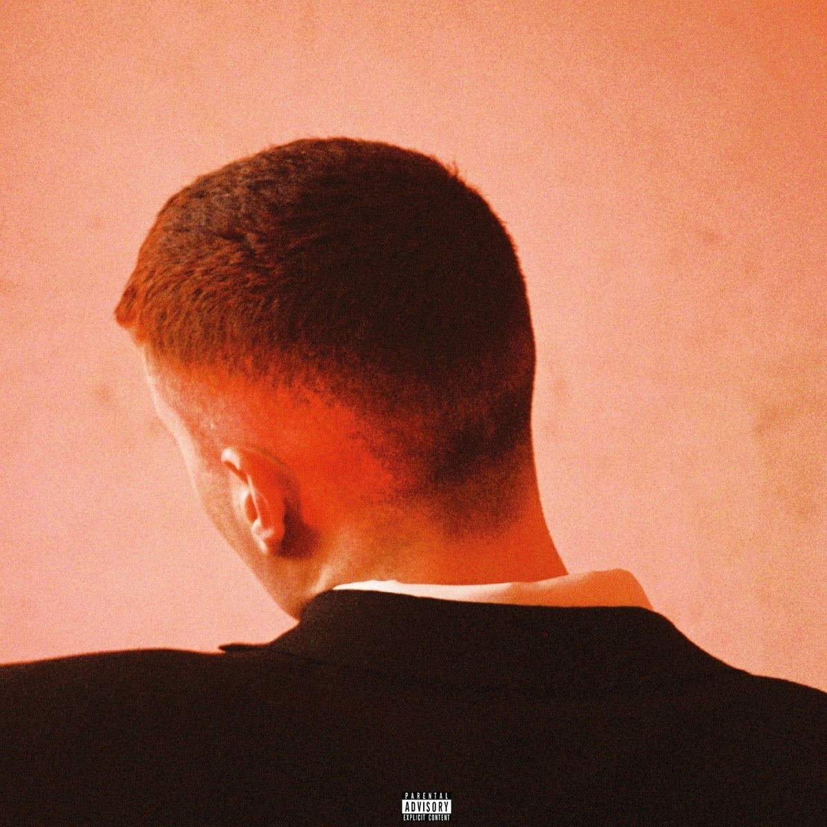 Back of a man's head with cropped hair against a warm pink wall