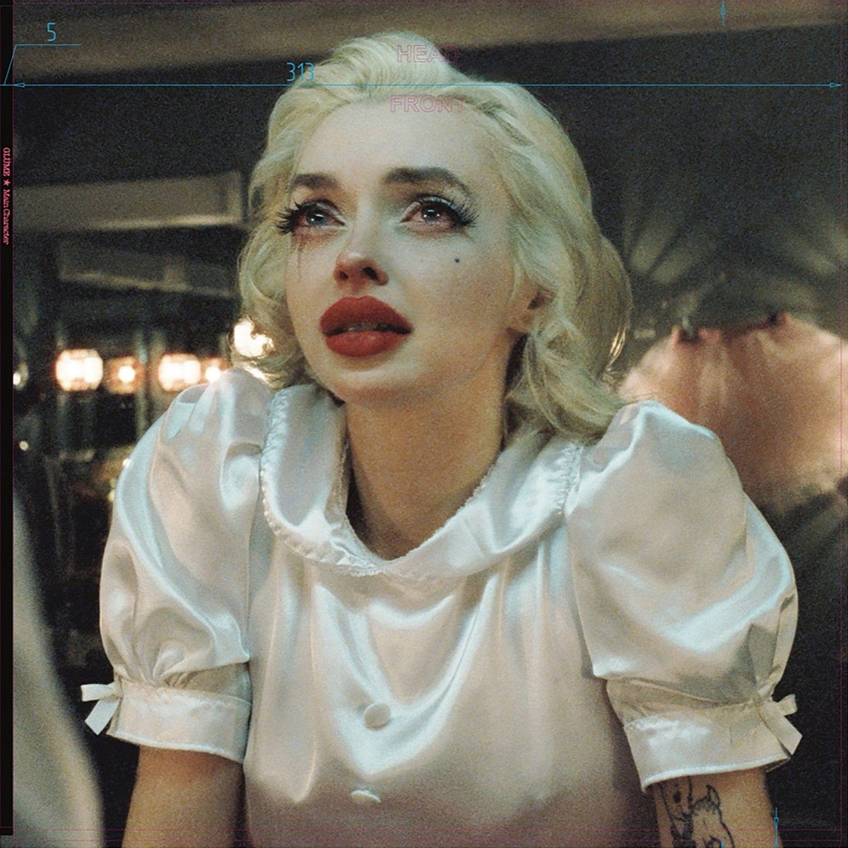 Woman with platinum curls and red lips in a white satin blouse, warm lights behind