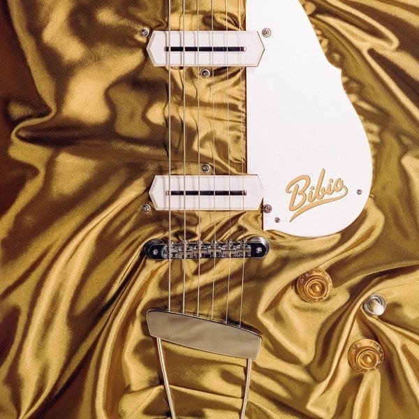 Close-up of an electric guitar body with cream pickups and scratchplate on gold satin fabric