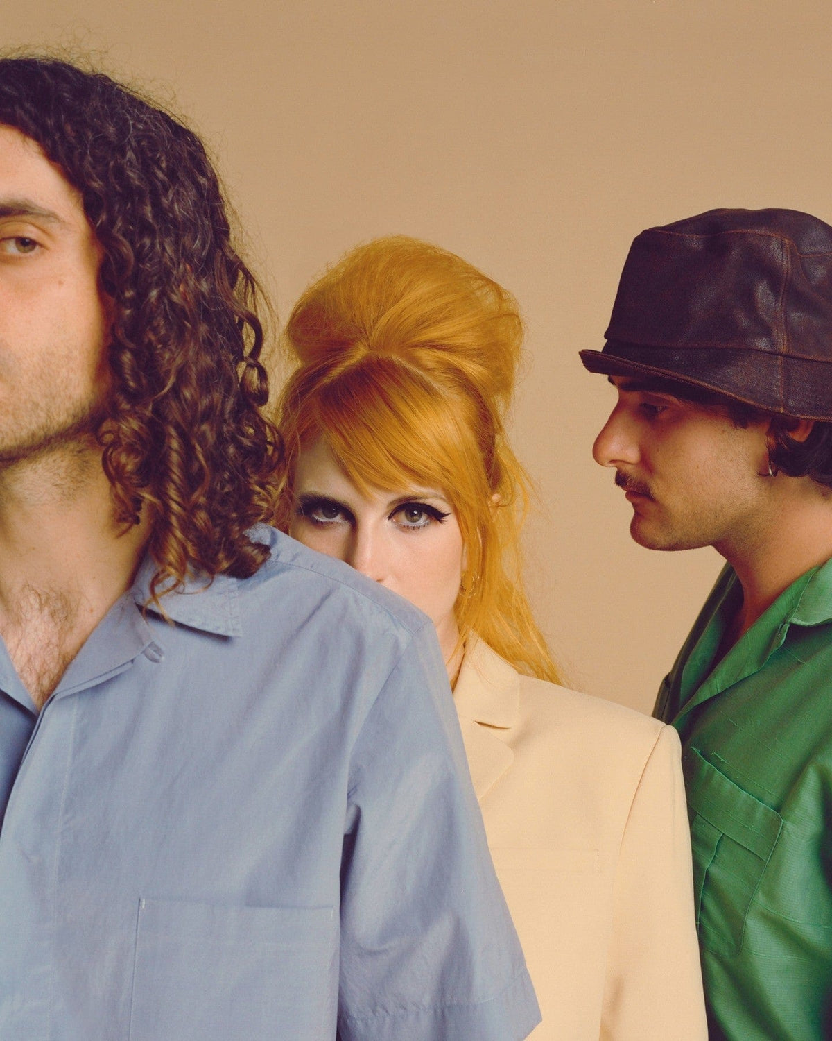 Three people posed against a beige backdrop, a woman with a red beehive between two men