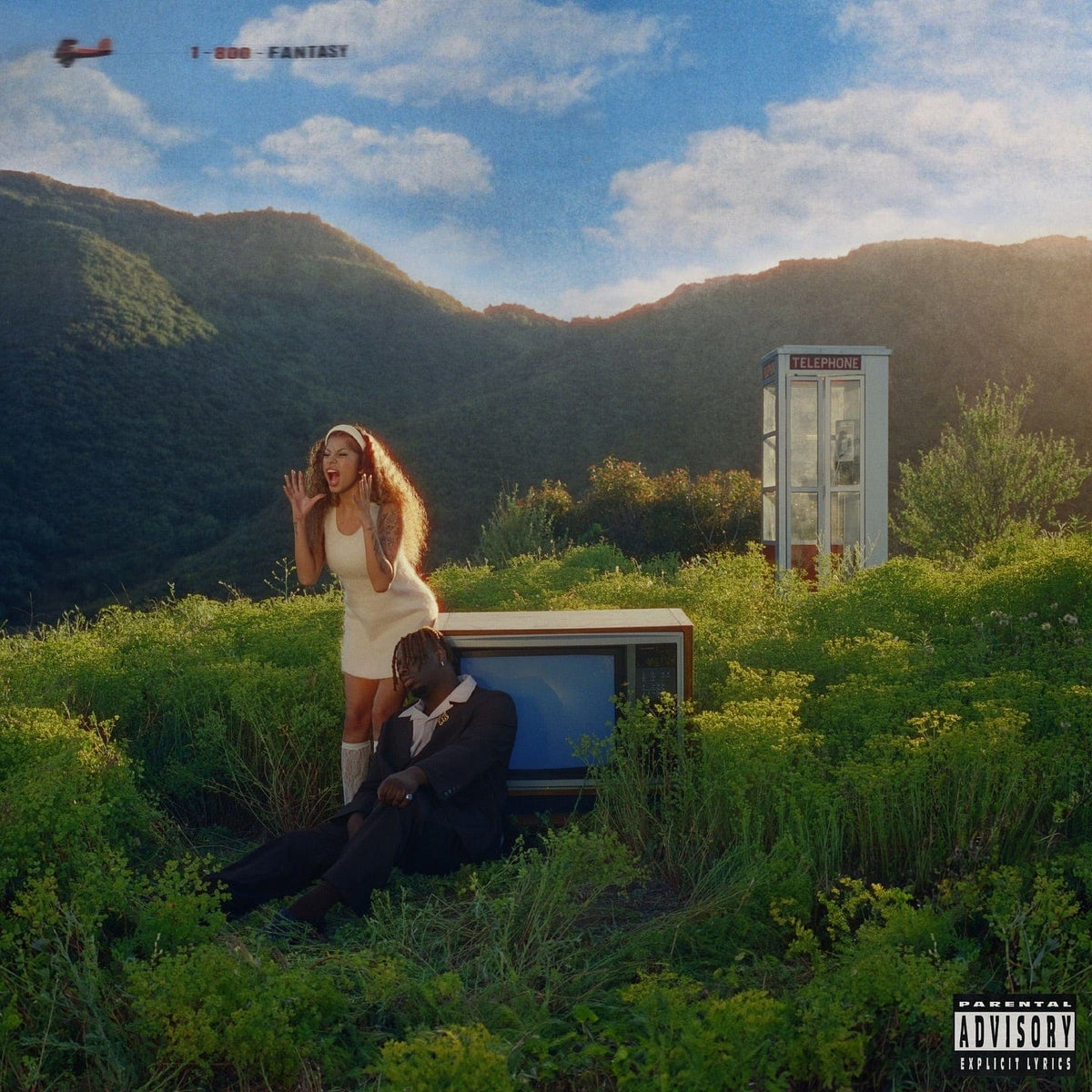 Woman and man beside an old television in long grass on a hillside, phone box behind
