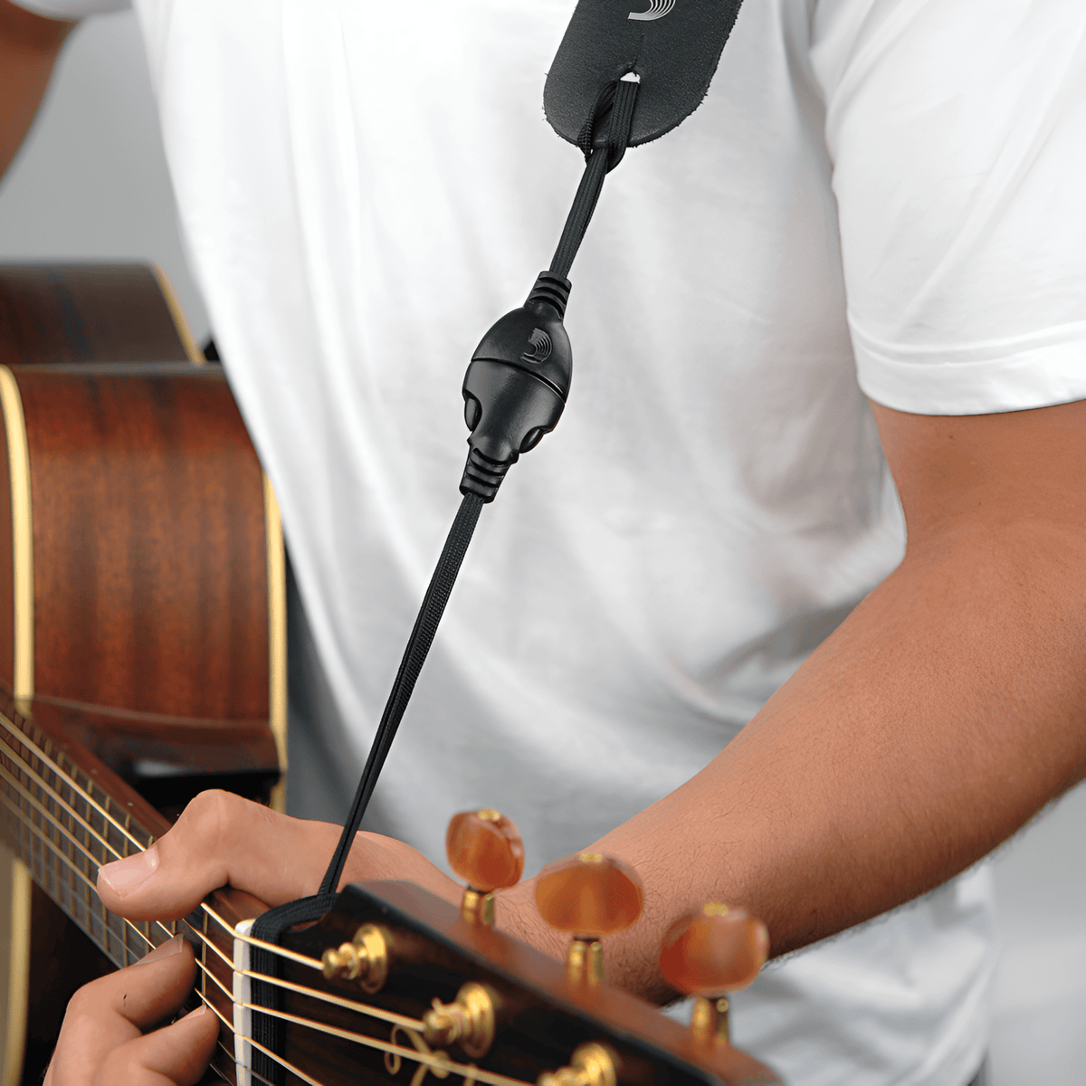 D'Addario DGS15 black quick-release cord looped around an acoustic guitar headstock and clipped to a black strap end