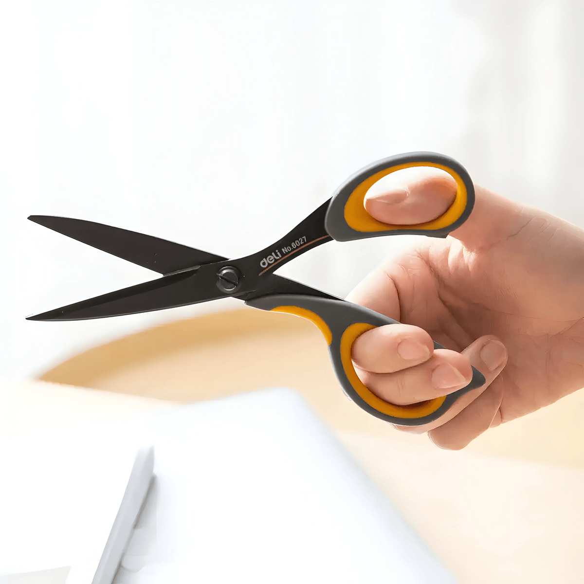 Deli E6027 scissors held open in a hand, showing the asymmetric grey and yellow grips