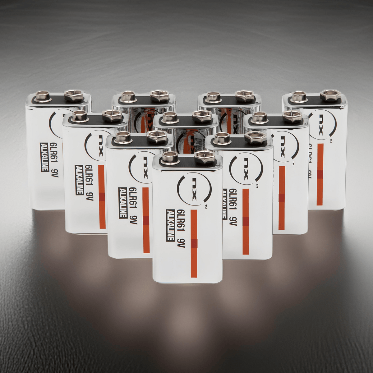 Ten NX 9V PP3 alkaline batteries arranged in rows on a dark reflective surface, labels facing forward