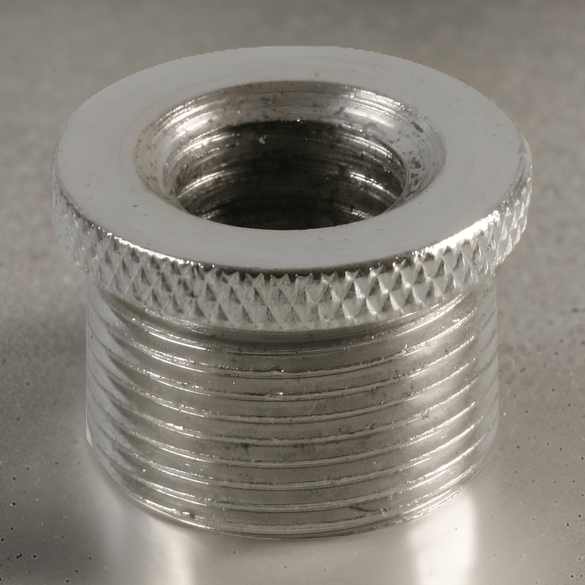 Pulse mic thread adaptor on a grey surface, looking into the 3/8" female inner thread past the knurled flange