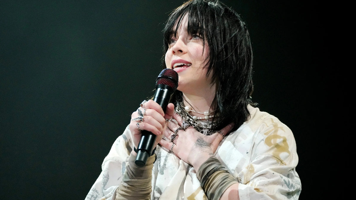 Performer on a dark stage holding a black handheld mic to her chest