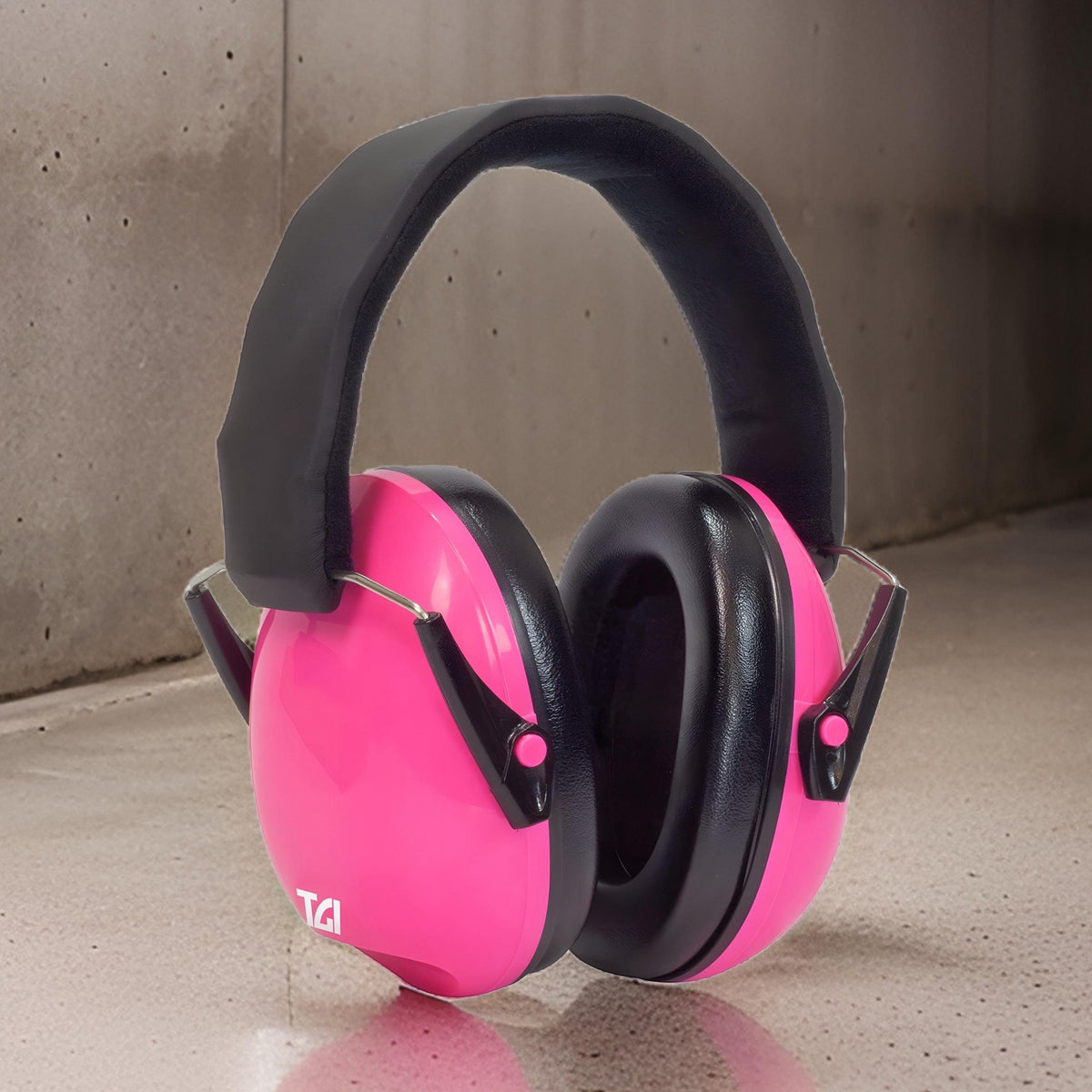 Pink TGI Junior Ear Defenders standing on a concrete floor against a concrete wall