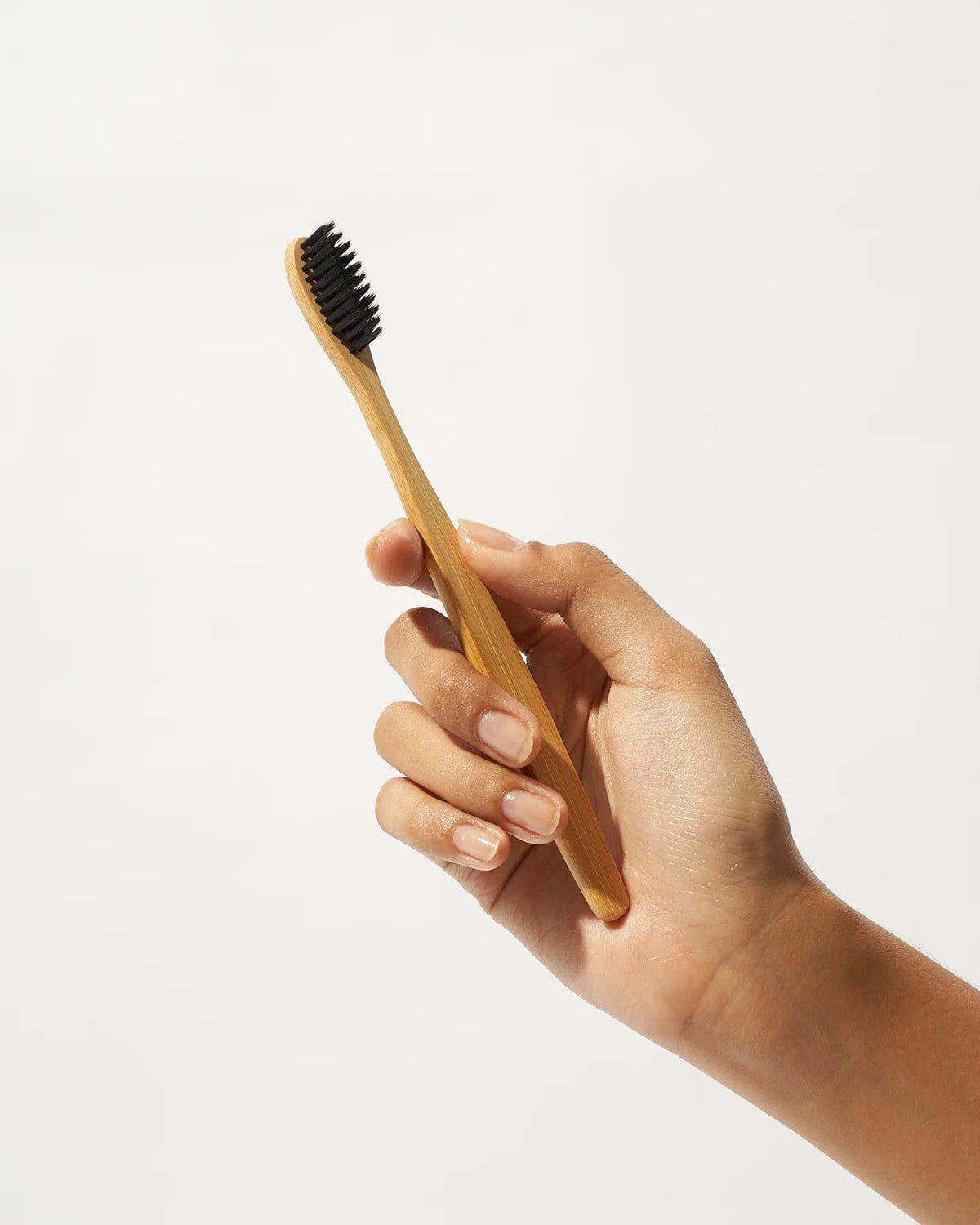 Bamboo toothbrush with soft black bristles held upright in a hand against a white background