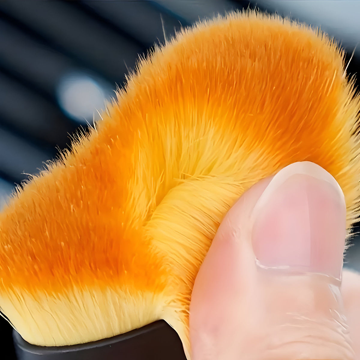 Close-up of the brush's dense, soft orange bristles with lighter tips, pressed down with a thumb