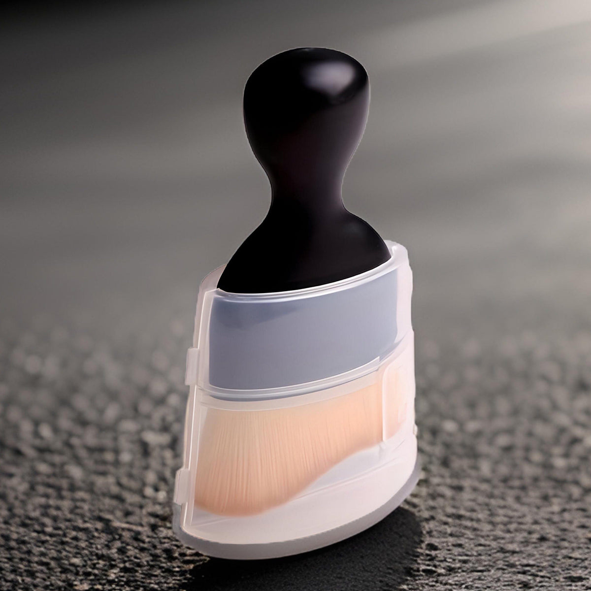 Dust brush in its clear protective cover standing on a dark textured surface, black knob handle on top