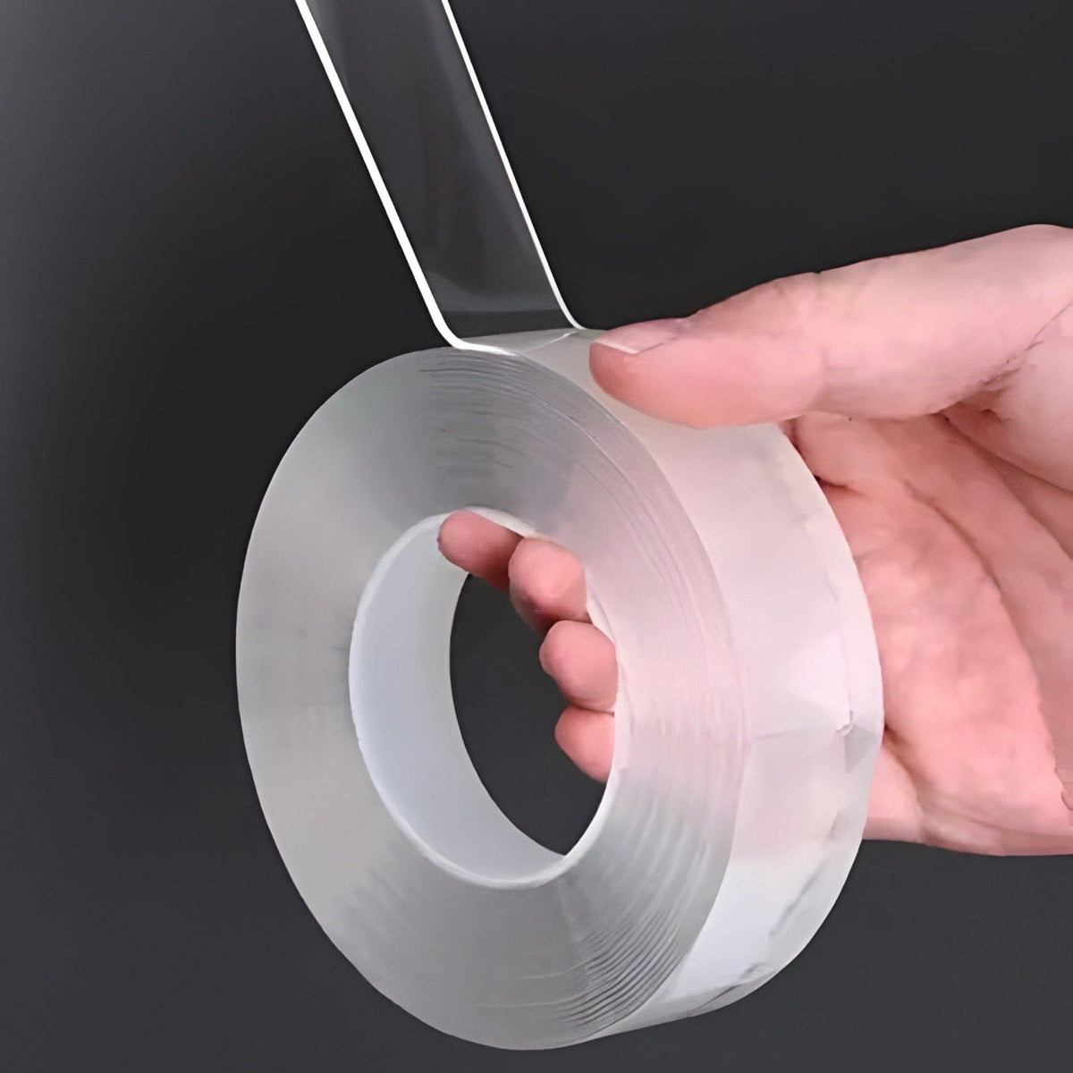 Transparent double sided tape roll held in a hand, a clear strip peeled up from the thick, gel-like roll