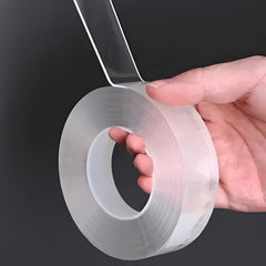 Transparent double sided tape roll held in a hand, a clear strip peeled up from the thick, gel-like roll
