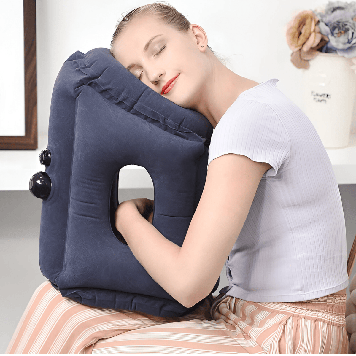 Woman resting forward on a navy version of the inflatable pillow on her lap, arms through the opening