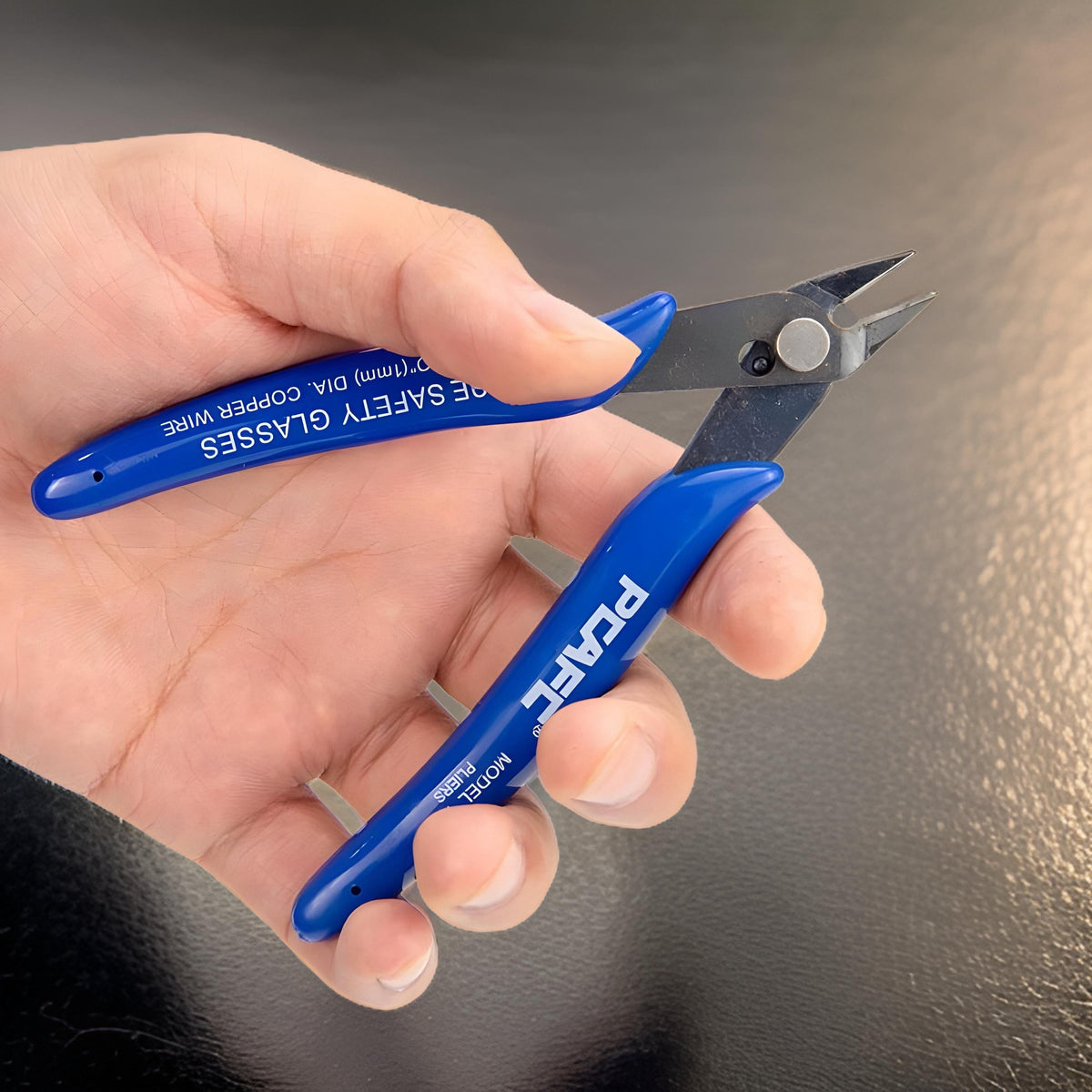 5 inch side cutters with blue grips held in a hand over a dark surface, handle printed Use Safety Glasses
