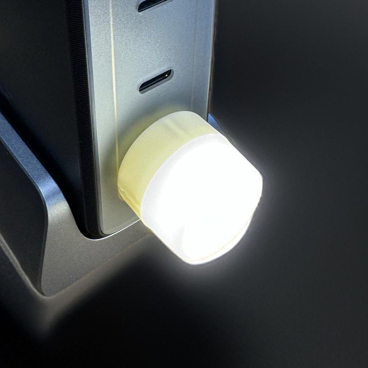 Mini USB LED night light plugged into the side USB port of a laptop, glowing brightly