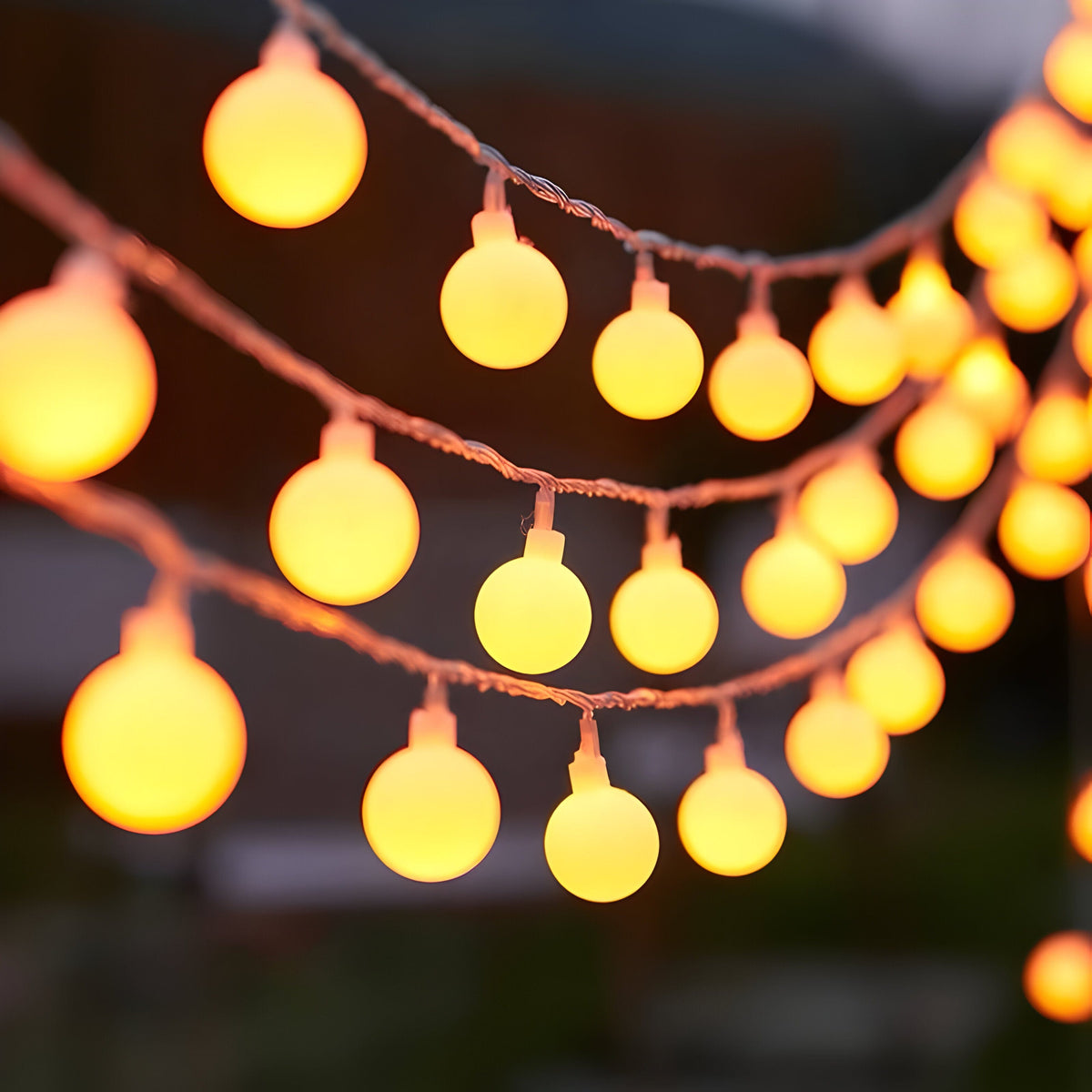 Close-up of glowing warm white globe string lights hanging in loops against a dark background
