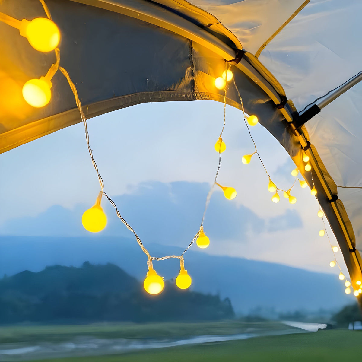 Warm white globe string lights hung round a tent doorway overlooking hills at dusk
