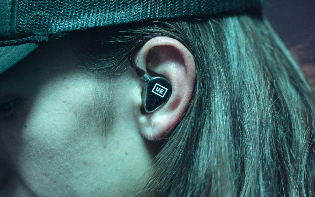 Musician in a cap wearing an Ultimate Ears universal in-ear monitor with UE logo faceplate
