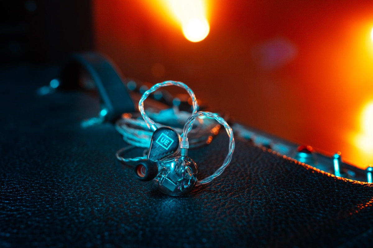 Ultimate Ears universal IEMs with clear cable resting on an amp under orange and teal stage lighting